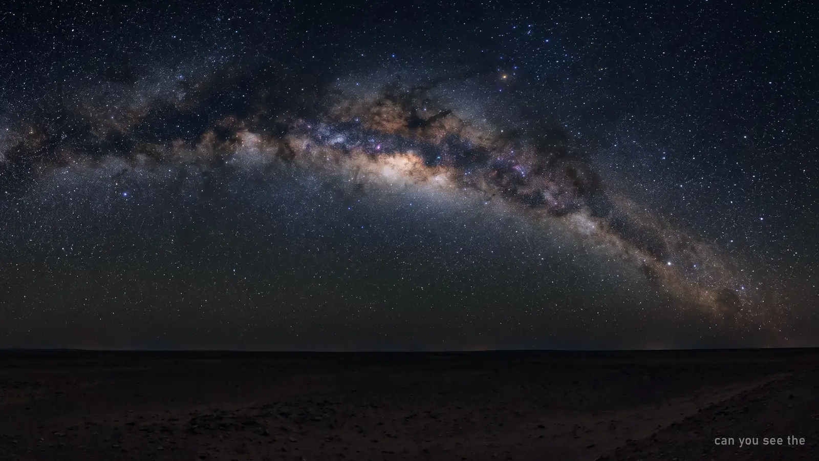 The Milky Way arching high overhead above a low dark desert horizon
