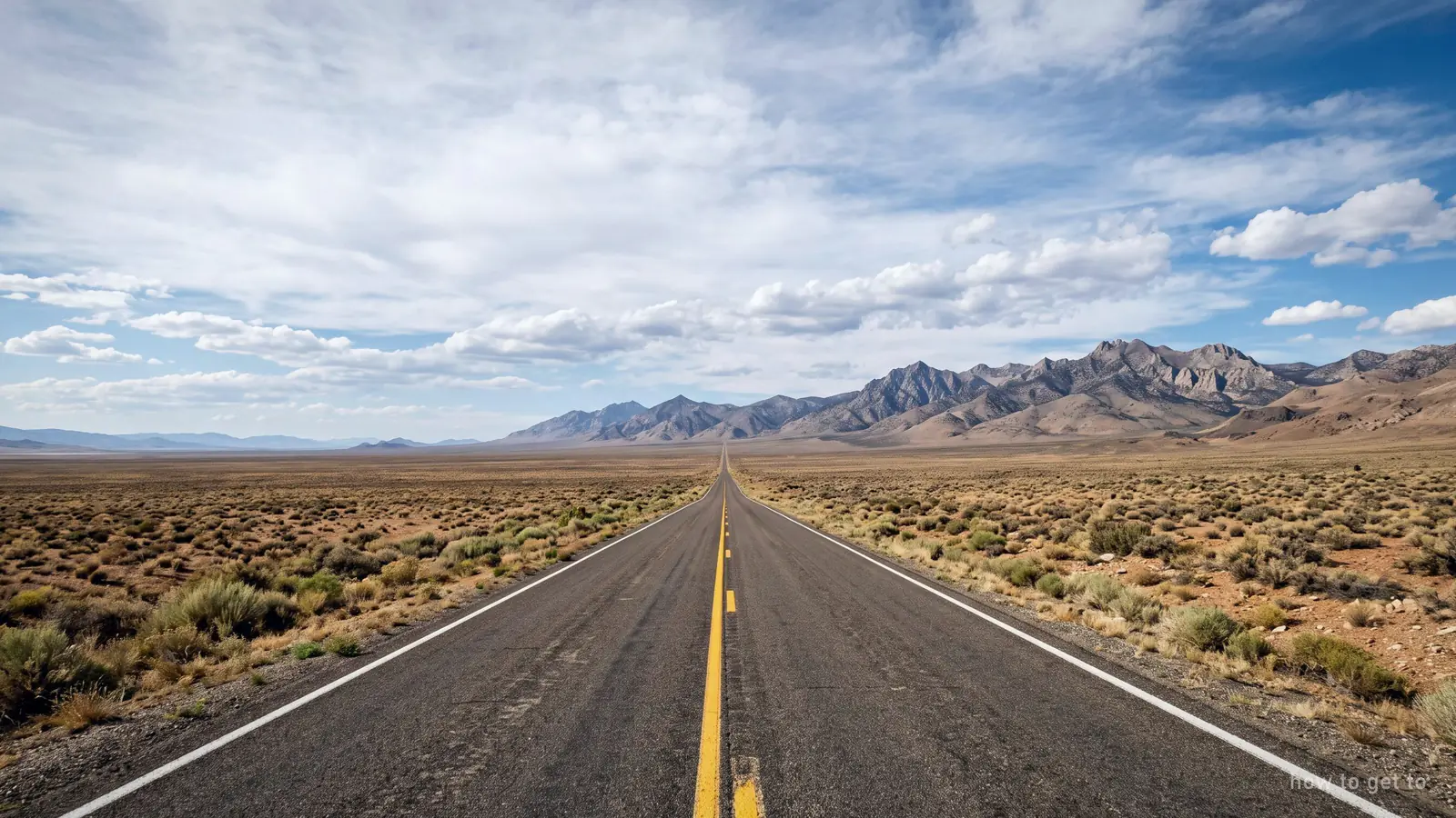 A straight desert highway running towards distant mountains under a wide sky