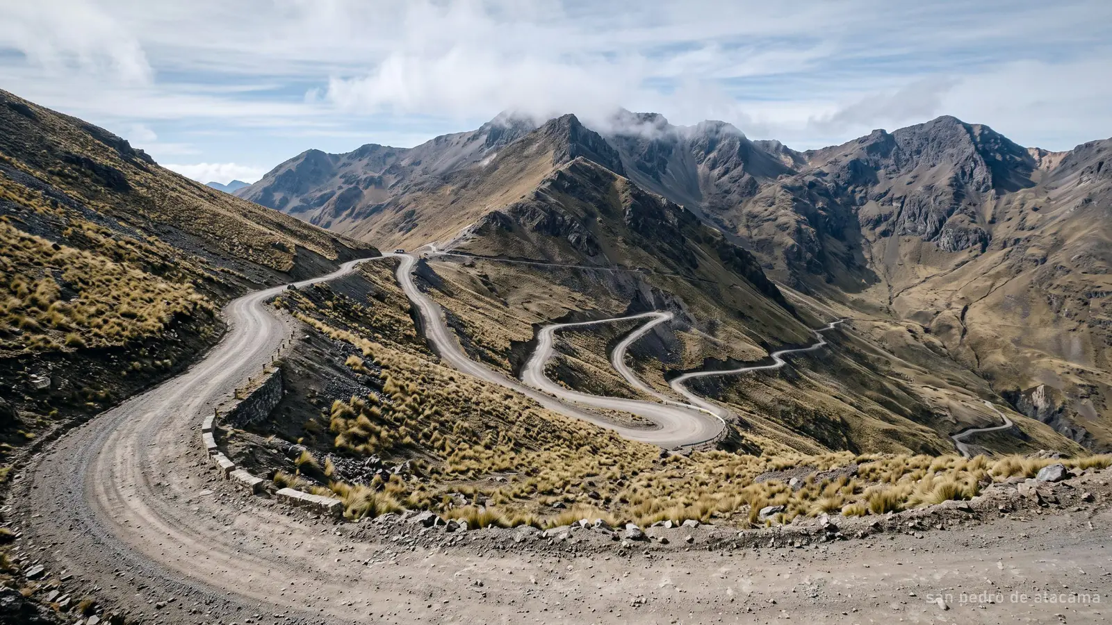 A gravel road climbing towards a high Andean pass with thin cloud over the ridge